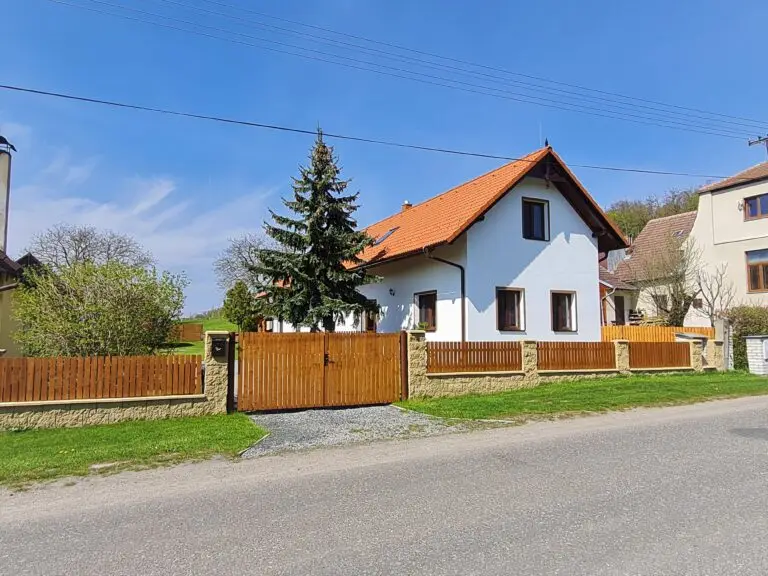 Pohled na chalupu z ulice s dřevěnou vjezdovou bránou