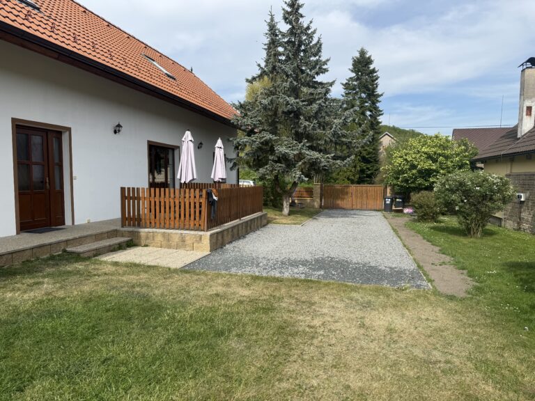 Průčelí chalupy s dřevěnou terasou a štěrkovým dvorem